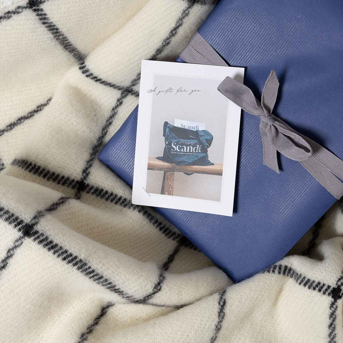 Wrapped magazine with a gray ribbon on a checkered blanket, accompanied by a Simply Scandi gift card